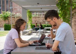 Studierende mit Laptops und Tablets an Tischen im Garten des Anglistischen Seminars.