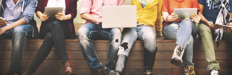 Studierende mit Laptops und Tablet auf Bank sitzend