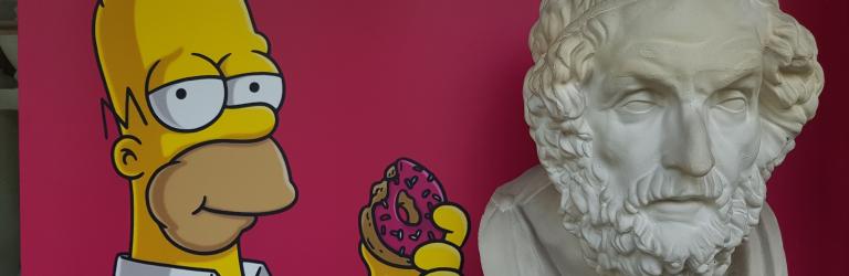 Das Foto zeigt Homer Simpson neben der antiken Büste Homers.