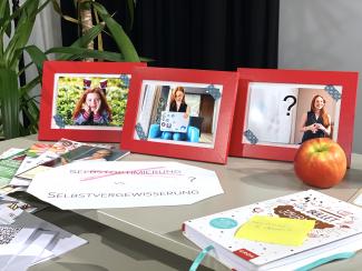 Schreibtisch mit Fotos aus verschiedenen Lebensphasen der Studierenden, Kladde, Apfel