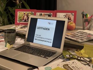 Schreibtisch mit auf aufgeklapptem Laptop und Leitfaden zum Portfolio