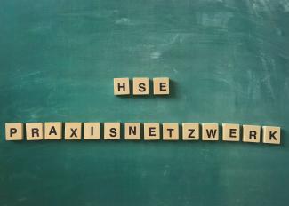 Schriftzug „HSE Praxisnetzwerk“ aus Holzklötzchen mit Buchstaben auf grünem Tafelhintergrund