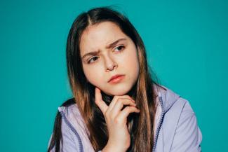 Vor petrolfarbenem Hintergrund ist eine junge Frau in nachdenklicher Pose abgebildet. Ihr Kinn ist auf ihre Hand gestützt. Bild: Pexels/KoolShooters