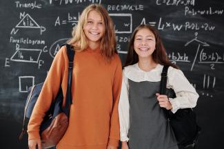 Zwei Mädchen stehen lachend vor einer Schultafel.