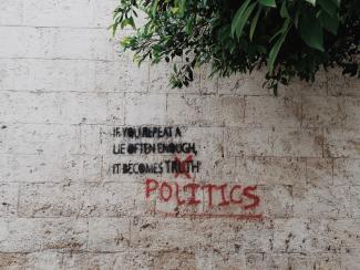 Graffitti auf einer Mauer mit dem Text: „If you repeat a lie often enough it becomes truth“. Das Wort „truth“ ist durchgestrichen und durch „politics“ ersetzt. 