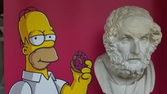 Das Foto zeigt Homer Simpson neben der antiken Büste Homers.