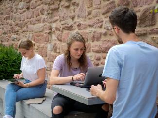 Studierende beim Arbeiten mit Laptop und Tablet im Garten des Anglistischen Seminars.