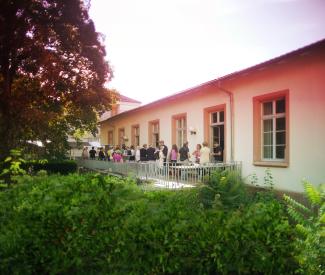 Das Bild zeigt viele Menschen im Gespräch auf der HSE-Terrasse im Abendrot, umgeben von Baum und Büschen.