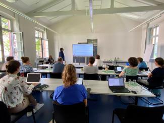 Im Konferenzraum der HSE stellen Dr. Thomas Renkert und Dr. Florian Nieser an einem Smartboard das Projekt ParzivAI vor. Im Vordergrund sind Teilnehmer:innen mit Laptops zu sehen.