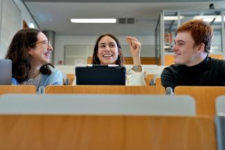 3 gutgelaunte Studierende im Hörsaal im angeregten Gespräch