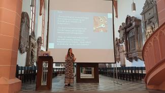Prof. Dr. Susanne Mantel bei ihrem Vortrag in der Akademischen Mittagspause am Pult der Peterskirche. Hinter ihr eine Folie mit dem Fazit ihres Vortrags.