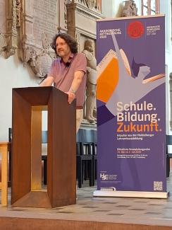 Prof. Dr. Michael Haus bei seinem Vortrag in der Akademischen Mittagspause am Pult der Peterskirche. Hinter ihm das Roll-up zur Akademischen Mittagspause.