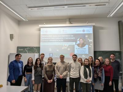 Gruppenbild mit Prof. Dr. René Venegas, Prof. Dr. Sibylle Große und Studierenden des Romanischen Seminars. Auf der Leinwand im Hintergrund der Vortragstitel „Análisis empírico de géneros discursivos y patrones léxico-gramaticales“