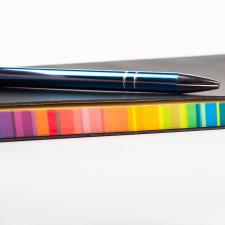 Ein Stift liegt auf einem Notizbuch mit schwarzem Einband und Buchschnitt in Regenbogenfarben