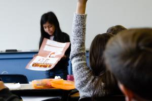 Ein dunkelhaariges Mädchen präsentiert im Unterricht ein Plakat; rechts im Vordergrund weitere Mitschüler:innen, eine meldet sich. | Bild: Taylor Wilcox | Unsplash