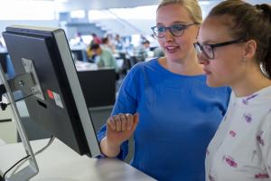 Zwei Studentinnen vor Computerbildschirm in der Bibliothek