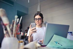 Studentin sitzt mit Laptop und Smartphone am Schreibtisch 