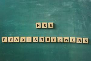 Schriftzug „HSE Praxisnetzwerk“ aus Holzklötzchen mit Buchstaben auf grünem Tafelhintergrund