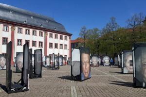 Aufnahme des Heidelberger Universitätsplatzes mit großformatigen Porträts von Überlebenden des Holocausts im Rahmen der Fotoausstellung „Gegen das Vergessen“ von Luigi Toscano; links im Bild die Alte Universität