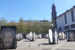 Aufnahme des Heidelberger Universitätsplatzes mit großformatigen Porträts von Überlebenden des Holocausts im Rahmen der Fotoausstellung „Gegen das Vergessen“ von Luigi Toscano; rechts im Bild die Neue Universität