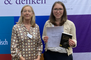 Das Bild zeigt Heidrun Dierk. Neben ihr steht Lena Muhn, die eine Urkunde und ein Buch in der Hand hält. Beide schauen freundlich in die Kamera.