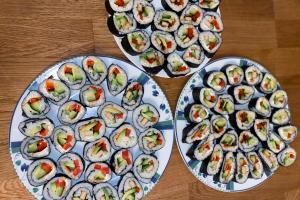 Das Bild zeigt drei Teller mit selbstgemachtem veganem Sushi auf einem Holztisch.