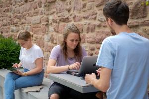 Studierende beim Arbeiten mit Laptop und Tablet im Garten des Anglistischen Seminars.