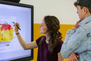 Eine Studentin markiert an einem Smartboard eine Grafik zur Erderwärmung. Neben ihr ein Kommilitone.