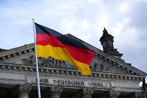Das Bild zeigt den oberen Teil des Reichstagsgebäudes mit der Inschrift DEM DEUTSCHEN VOLKE, davor eine Deutschlandfahne. 