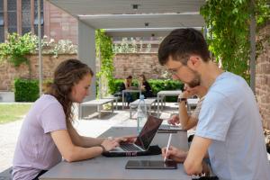 Studierende mit Laptops und Tablets an Tischen im Garten des Anglistischen Seminars.
