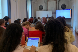 Studierende sitzen, z. T. mit Tablets, eng aneinandergedrängt in einem opulenten Altbau der Università degli Studi di Milano. Vorne sind Smart Screens zu erkennen.