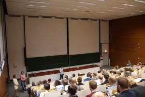 Prof. Dr. Claudia Hildebrandt eröffnet den Heidelberger Informatiklehrkräftetag im vollen Hörsaal. Seitlich neben ihr sind Prof. Dr. Karin Vach (Rektorin PH Heidelberg), Prof. Dr. Silke Hertel (Prorektorin für Studium und Lehre, Universität Heidelberg) und Eleonore Dietrich (Deutsche Gesellschaft für Informatik, ILL-BW) zu erkennen.