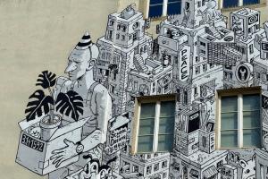 Das Foto zeigt den Ausschnitt eines Murals der Künstlergruppe WENU auf der Außenwand des Kurfürst-Friedrich-Gymnasiums. Abgebildet ist eine urbane Gebäudelandschaft mit stilisierten Schul-Elementen sowie Schriftzügen wie "School of Dreams", "Peace" oder "Love".