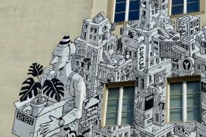 Das Foto zeigt den Ausschnitt eines Murals der Künstlergruppe WENU auf der Außenwand des Kurfürst-Friedrich-Gymnasiums. Abgebildet ist eine urbane Gebäudelandschaft mit stilisierten Schul-Elementen sowie Schriftzügen wie "School of Dreams", "Peace" oder "Love".