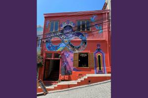 Das Bild zeigt ein rotes Haus mit buntem Mural auf einer Straße in Hanglage in Valparaiso. Der Himmel darüber ist strahlend blau.