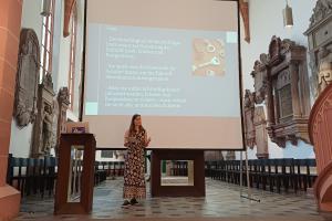 Prof. Dr. Susanne Mantel bei ihrem Vortrag in der Akademischen Mittagspause am Pult der Peterskirche. Hinter ihr eine Folie mit dem Fazit ihres Vortrags.