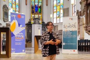 Dr. Nicole Aeschbach bei ihrem Vortrag in der Akademischen Mittagspause am Pult der Peterskirche. Hinter ihr das Roll-up zur Akademischen Mittagspause und die Buntglasfenster der Peterskirche..