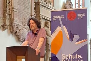 Prof. Dr. Michael Haus bei seinem Vortrag in der Akademischen Mittagspause am Pult der Peterskirche. Hinter ihm das Roll-up zur Akademischen Mittagspause.