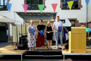 Die drei Preisträgerinnen stehen – gemeinsam mit Vera Heyl – auf einer Bühne, und halten ihre Urkunden in der Hand.