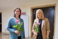 Die Lehrerinnen Miriam Wedekind und Laura Klas vor einem Seminarraum; beide halten eine rosafarbene Rose in der Hand.