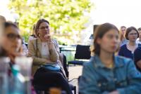 Blick ins Publikum der Terrassengespräche während des Vortrags. Im Fokus Prof. Dr. Marita Friesen in nachdenklicher Haltung, um sie herum Studierende. Im Hintergrund ein Baum.