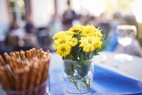 Gelbe Blumen und Salzstangen auf einem Tisch auf der HSE-Terrasse. Im Hintergrund sind schemenhaft Veranstaltungsgäste zu erkennen.