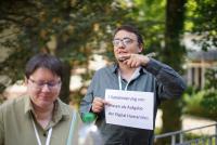 Dr. Thomas Renkert hält beim ersten Cluster-Forum des Forschungs- und Transferclusters „Kulturelles Erbe und Kanonisierung von Wissen“ ein Schild in der Hand, auf dem zu lesen ist: „2 – Kanonisierung von Wissen als Aufgabe der Digital Humanities“