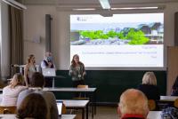 Die Vortragenden der Uni Trier bei ihrem Pitch zu TrigitalPro. Hinter ihnen die Leinwand mit Projektinformationen, im Vordergrund Köpfe von Zuhörenden. Bild: © Heidelberg School of Education | Vanessa Bender