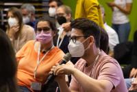 Ein Teilnehmer mit Maske und Mikrofon richtet eine Frage an die Diskutant:innen auf dem Podium. Bild: © Heidelberg School of Education | Vanessa Bender