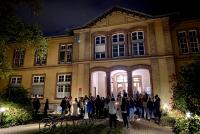 Unter dem Nachthimmel stehen im Hof des Psychologischen Instituts zahlreiche Vortragsbesucher:innen beim abendlichen Umtrunk zusammen.