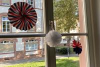 Sprossenfenster mit Pompoms und Girlanden im USA.Stil; dahinter ist der Campus Bergheim im Sonnenschein zu erkennen.