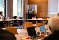 Prof. Dr. Felicitas Thiel bei ihrem Impulsvortrag. Im Vordergrund sind in U-Form sitzend Teilnehmende des Lehrkräfteverbunds mit Laptops zu erkennen.