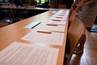 Auf einer langen Tischreihe ist die ausgedruckte Gründungserklärung zur Unterschrift ausgelegt. Auf den Blättern liegen Stifte bereit.