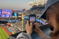 Eine junge Frau mit Baseball-Cap macht im voll besetzten Stadion ein Foto mit ihrem Smartphone. Die Ränge sind mit Zuschauern gefüllt.